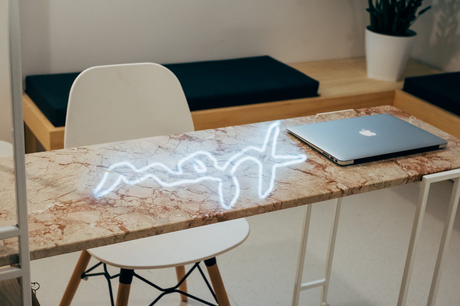The neon sign reflected in the pink-veined marble of the reception desk, next to a laptop